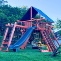 Green wooden playset with a slide in a backyard setting