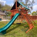 Children's playground with green slide and wooden structure in a backyard setting.