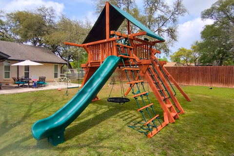 Children's playground with green slide and wooden structure in a backyard setting.