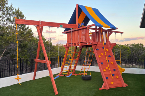 Children's playground with red swing set and climbing structure on a grassy area.