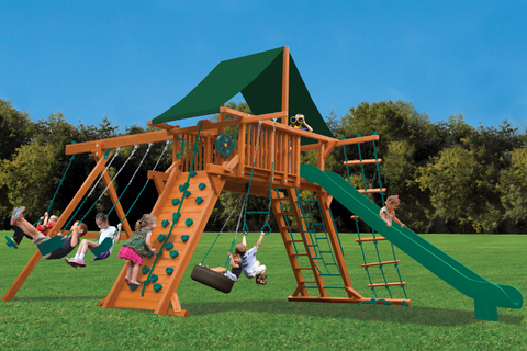 Children playing on a wooden playground set with swings, slides, and climbing structures.