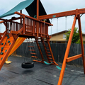 Wooden playground set with slides and swings in a backyard setting.