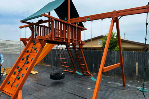Wooden playground set with slides and swings in a backyard setting.